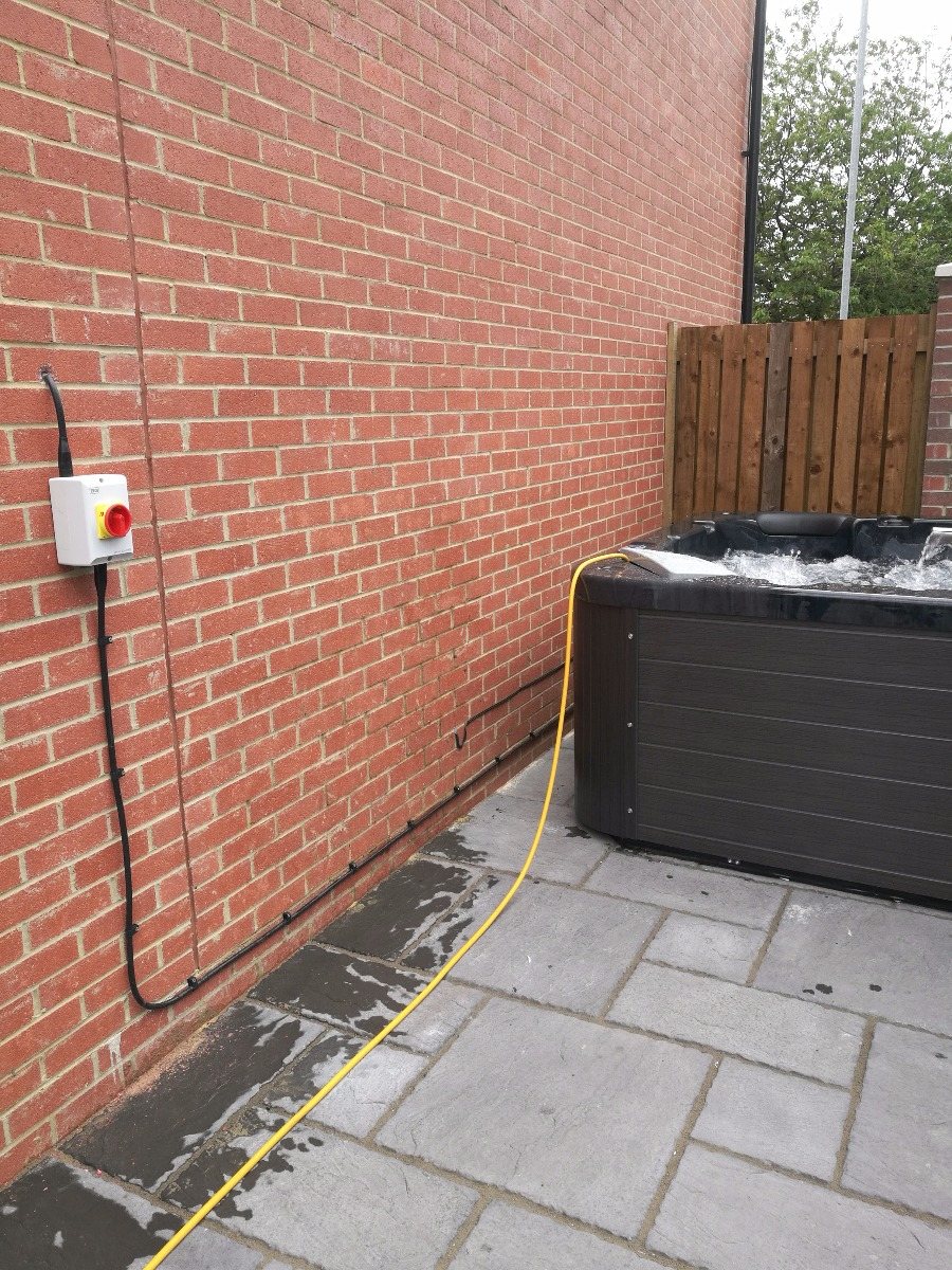 A weatherproof isolator switch on a brick wall with a neat cable run down to a newly installed hot tub